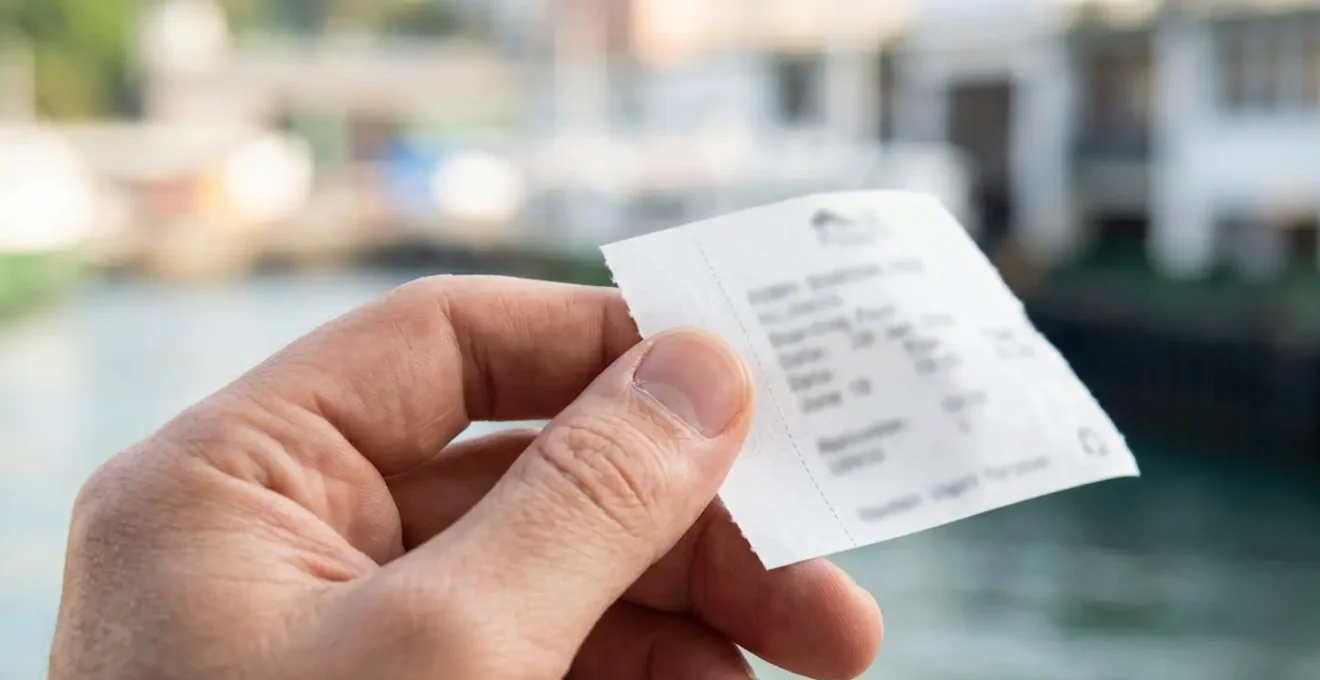 Gros plan macro sur une main tenant un billet de ferry avec texture papier nette et arrière-plan flouté aux tons doux